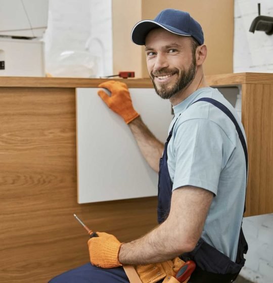 cheerful-male-worker-fixing-cupboard-door-in-kitchen.jpg